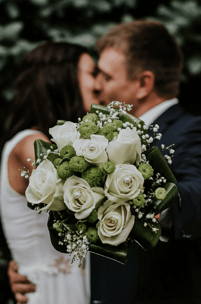 Bride and groom kissing, focus on white and green bouquet.
