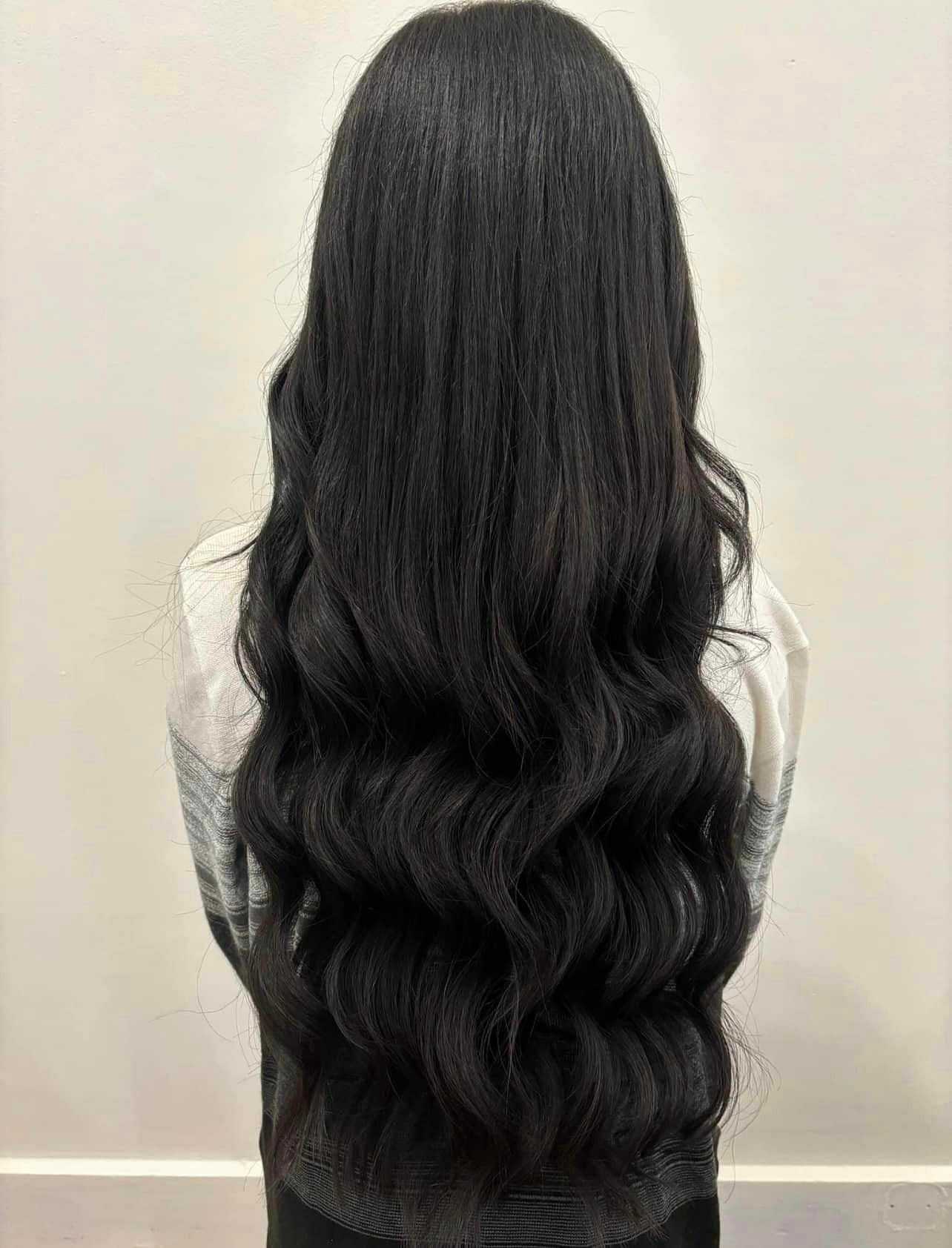 Woman with long, wavy, dark hair seen from the back, wearing a light-colored top.
