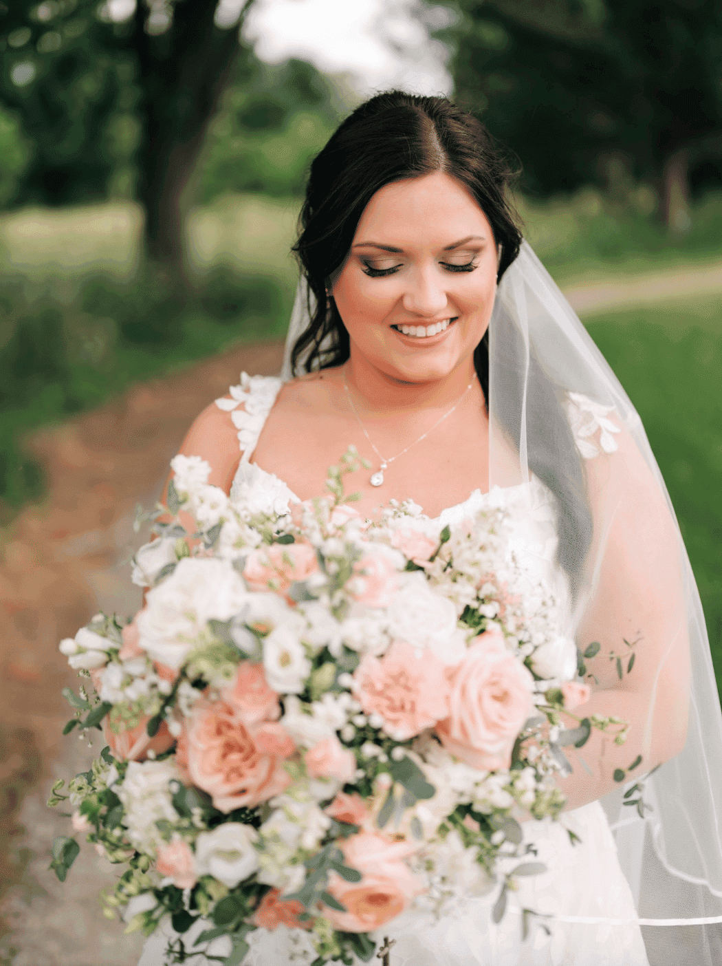 Bride holding a large bouquet of pink and white flowers outdoors.