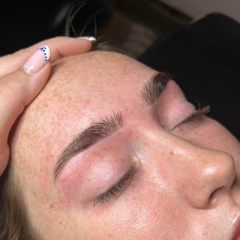 Close-up of a woman's face with groomed eyebrows, eyes closed, and a hand touching her forehead.
