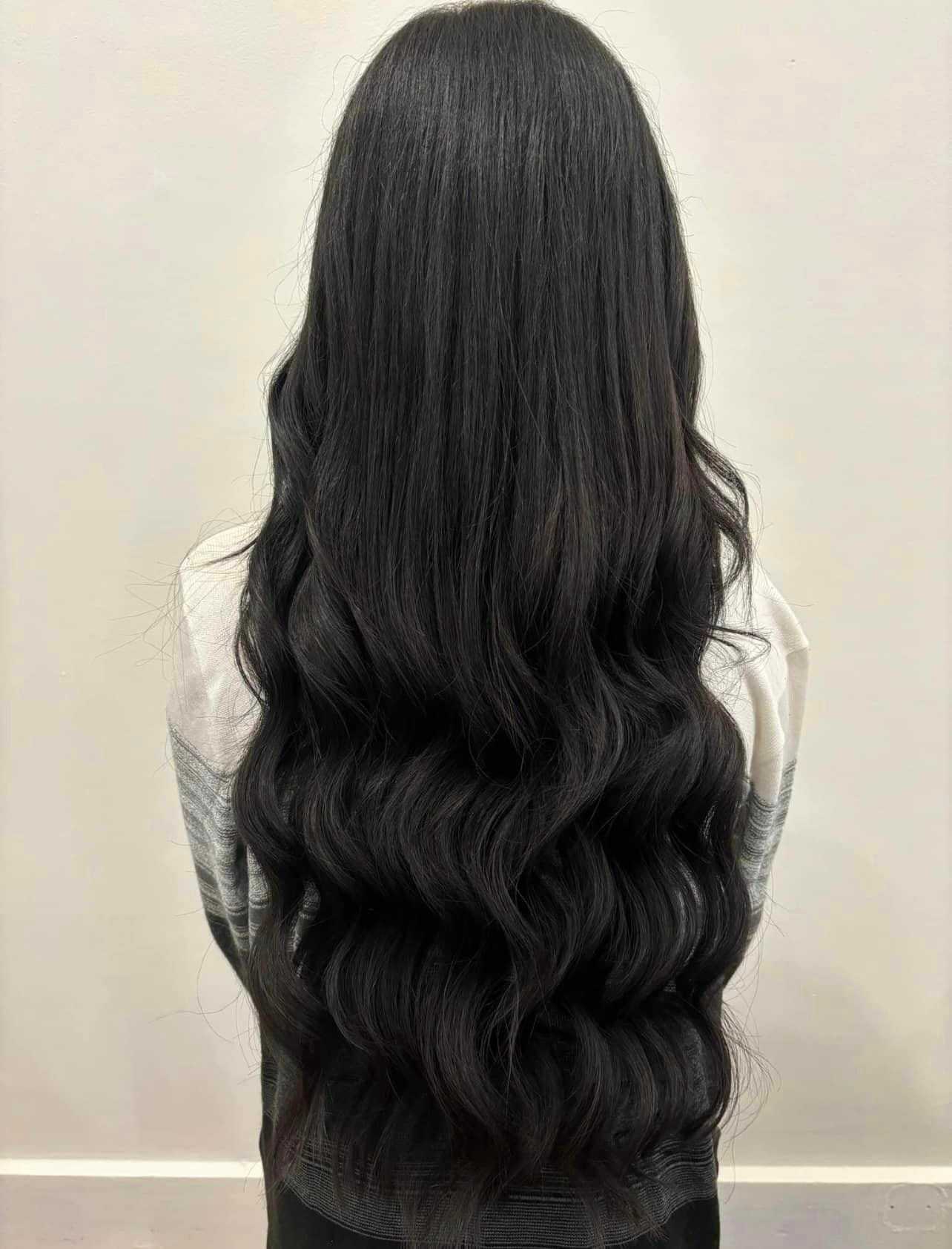 Woman with long, wavy, dark hair seen from the back, wearing a light-colored top.