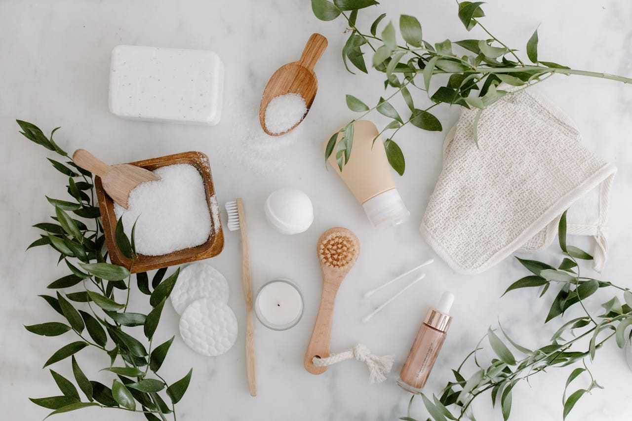 Various spa items including brushes, soap, and greenery arranged on a white background.