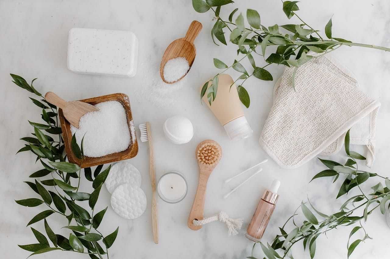 Various spa items including brushes, soap, and greenery arranged on a white background.