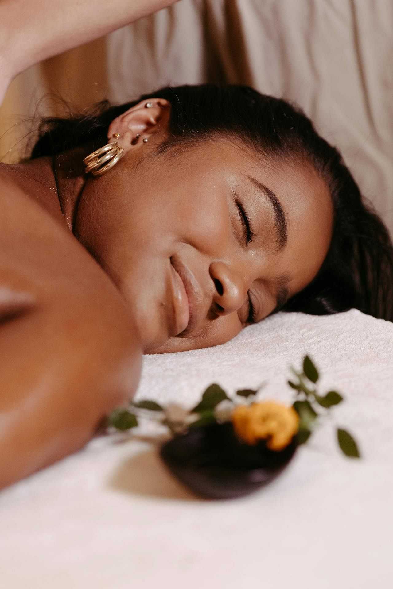 Woman relaxing with her eyes closed during a spa session, with a flower and leaves nearby.