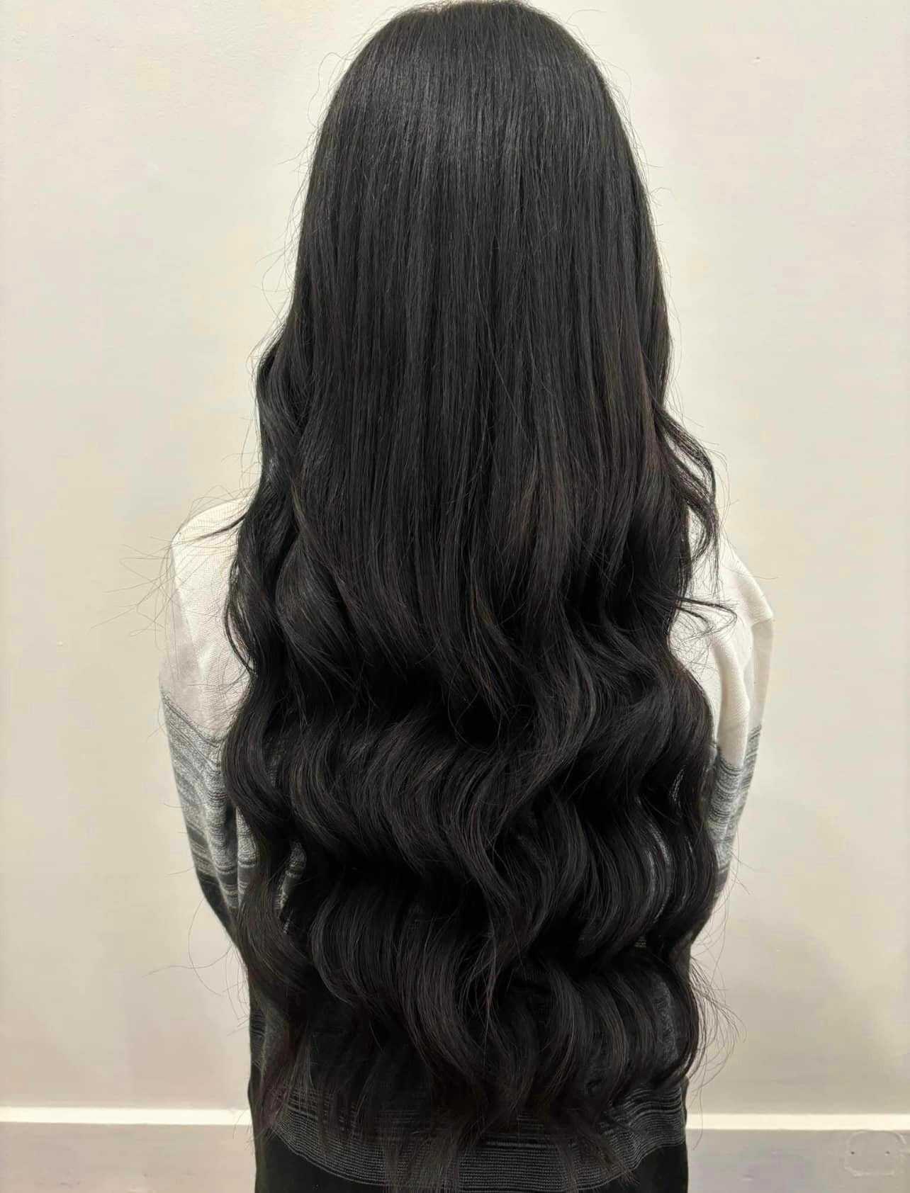 Woman with long, wavy, dark hair seen from the back, wearing a light-colored top.