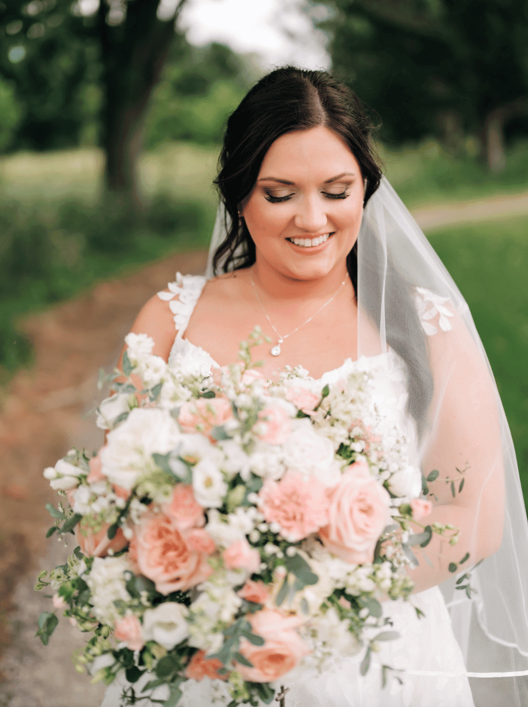 Bride holding a large bouquet of pink and white flowers outdoors.